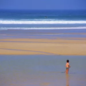 Enfant sous le soleil à la plage, au loin un surfeur dans les vagues